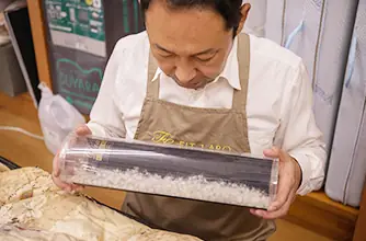 透明な筒に入った羽毛を見つめる店主